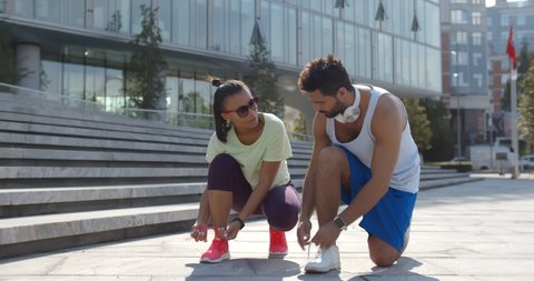 Diverse couple lacing shoes before training outdoors. Portrait of young Indian man and woman in sportswear exercise together in city