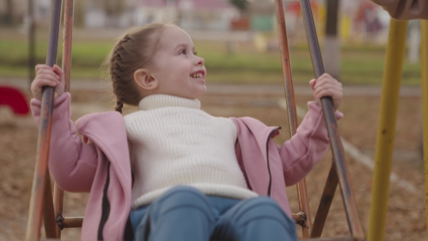 mother pushes the swing up and cheerful child laughs, happy family, kid play on the swing in autumn playground, children's entertainment outside, life of little people on weekends, chidhood dream fly. Royalty-Free Stock Footage #1087085411