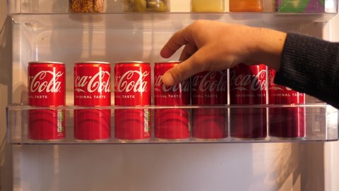 WROCLAW, POLAND - FEB 16, 2022: Person takes a can of cola from the fridge door shelf