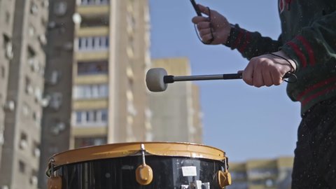 Male hands begin to beat the drum, water is poured onto the drum and sprayed. Drumming and splashing water in slow motion