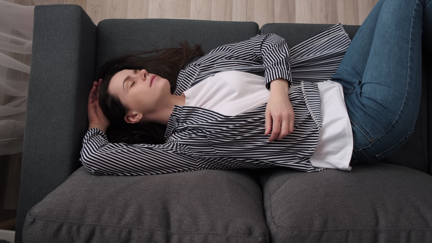 Top view of exhausted or bored young sleepy woman falls down on sofa. Apathetic tired lazy female sleeping on grey couch at home alone. Girl lying asleep feeling lack of motivation, fatigue concept | Shutterstock HD Video #1087087928
