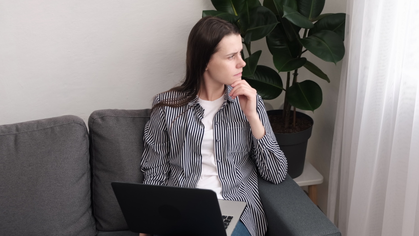 Thoughtful concerned young woman sit on sofa working on laptop computer looking away thinking solving problem at home, serious female 20s search for inspiration make decision feel lack of ideas Royalty-Free Stock Footage #1087088861