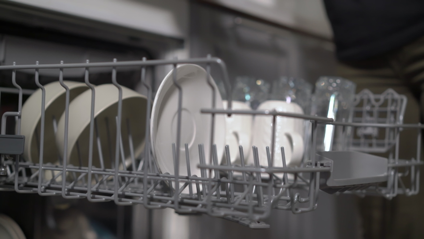 Young woman in the kitchen opens the dishwasher, loads and takes out dishes. The girl washes the plates and cups. Cleaning, housework, housewife. | Shutterstock HD Video #1087089113