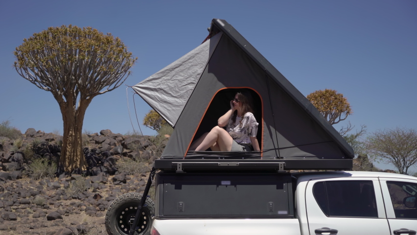SUV car with camping equipment, rooftop tent, spare tire. A white pickup truck parked in savannah. Travel and adventure in desert of Namibia, Africa. Quiver tree forest in Keetmanshoop. Woman in camp.
