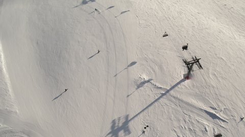 Skier skiing downhill in winter resort mountains. Aerial top view of ski area with marks and working chairlifts. Skiers and snowboarders riding down the hill. 4k ProRes 422