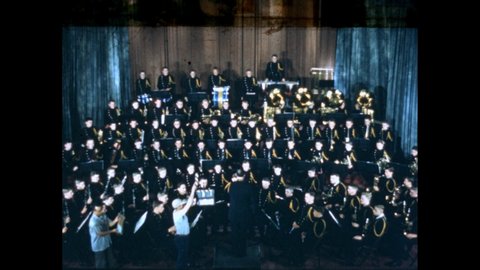 1950s: People holding clapperboards, clapping. Clapperboard breaking. Orchestra playing instruments on stage. Conductor conducting band. Musicians playing instruments.