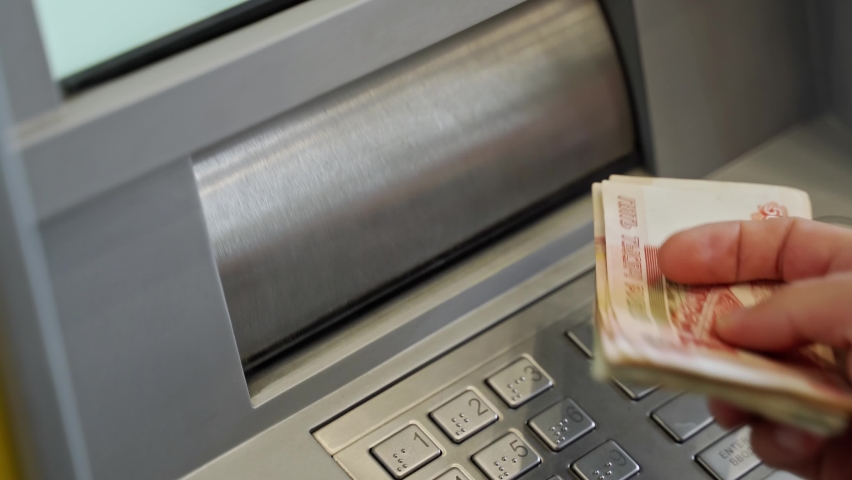 Close-up of a man's hand puts a wad of cash into the receiving slot of an ATM. The dispenser closes after receiving the money. depositing paper money into an ATM. replenishment of the account in cash | Shutterstock HD Video #1087098443