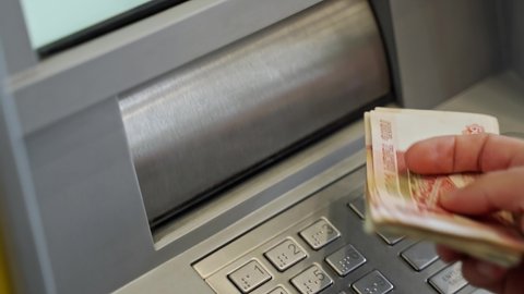 close-up of a man's hand puts a wad of cash into the receiving slot of an ATM. The dispenser closes after receiving the money. depositing paper money into an ATM. replenishment of the account in cash