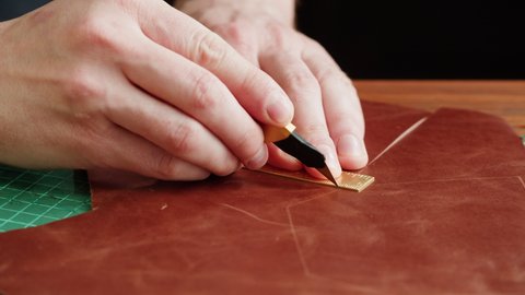 Man tailor cutting artificial leather with ruler close-up. Craftsman carving cowhide at workplace table, making hand made products made of genuine animal leather. Professional atelier.