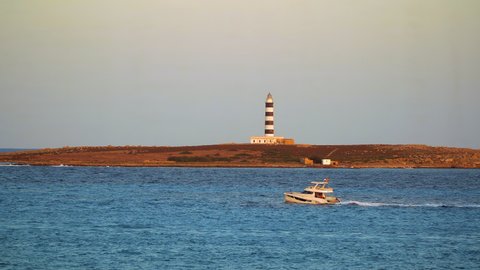 Punta Prima, Menorca - Spain - August 30 2021: Boat crossing in front of the Illa de l'Aire lighthouse in Punta Prima, Menorca.