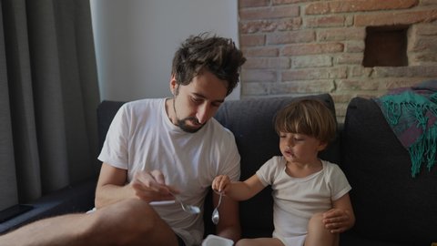 Candid family moment father feeds toddler child yogurt breakfast in morning