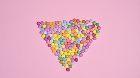 6k Colorful rainbow candies make heart shape on pastel pink background. Stop motion flat lay