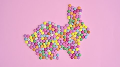 6k Colorful sweet candies make Easter bunny shape on pastel bright pink background. Stop motion flat lay concept