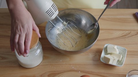Woman is cooking some bakery for her family, adding sugar to mixed eggs, preparing dough, Foreground.