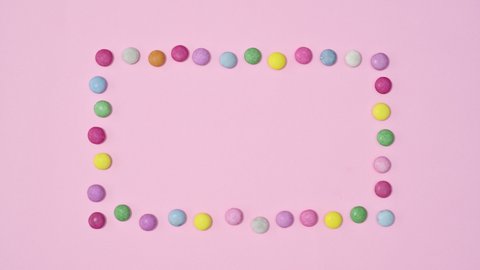 6k Creative arrangement of colorful rainbow candies frame on pastel pink background. Stop motion. Flat lay minimal