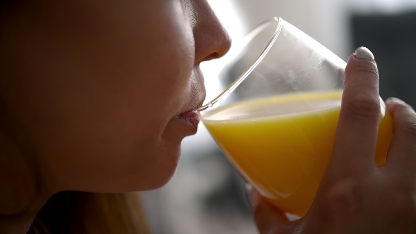 Female drinking yellow juice detox cocktail. Close-up person is tasting orange juice in a glass and enjoying the drink in the morning. Fitness and healthy lifestyle concept.