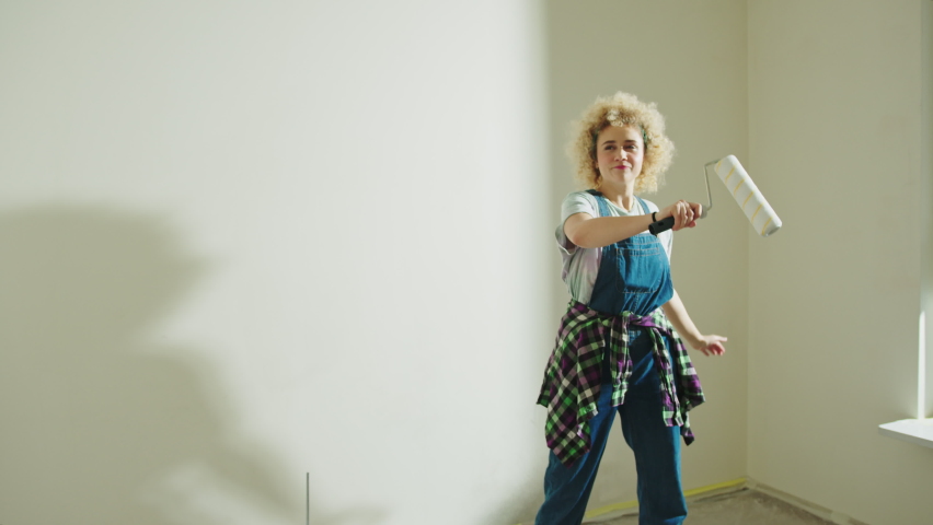Young satisfied girl makes repairs in the apartment Paint Roller. wall painting concept