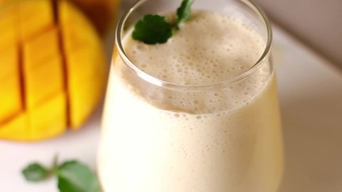 A metal drinking straw is placed in a glass of Indian drink lassie. Milk, mango, yogurt, mint.