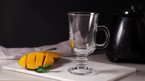 Traditional Indian drink lassie,wiith mango is poured into a glass, mango on the board, mint leaf, blender. Yogrut, milk, mango.