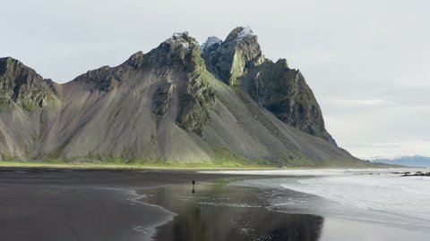 Drone Shot Of Man On Black Sand Beach With Tide Coming In As He Runs Towards Vestrahorn Mountain, Iceland
