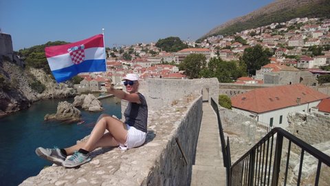 Woman with Croatian flag on Dubrovnik city walls of Croatia. View of Fort Lovrijenac fortress, and the West Harbour. Dubrovnik UNESCO World Heritage Site is an old Venetian city of Croatia in Dalmatia