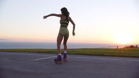 Idyllic natural summer landscape with beautiful sunset skyline and ocean view. Beautiful and healthy woman riding roller skates in the park within seascape. High quality 4k footage