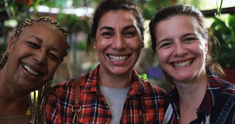 Multiracial women working together inside nursery greenhouse while smiling on camera - Green market concept