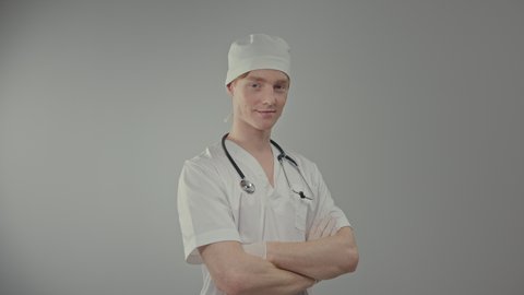 Young Doctor In Medical Gown And Gloves. Man Puts Stethoscope Around His Neck And Puts His Hands On His Chest. Smiling Guy.