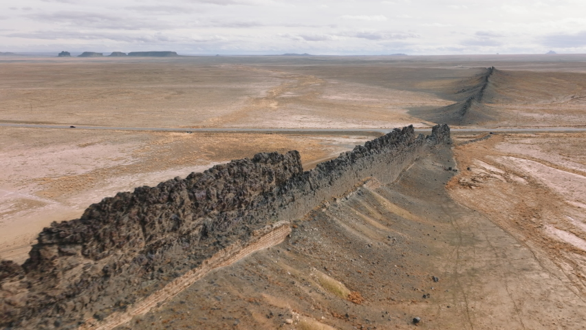 Aerial footage of the enormous, long stone range, stretching along vast desert. Vehicles drive within National reserved area around Ship Rock, New Mexico with barren landscape. High quality 4k footage