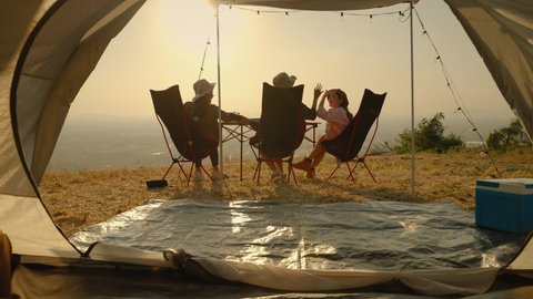 group of young Asian friends playing guitar and singing in a tent during a summer camping vacation. concept of freedom, leisure, travel, adventure
