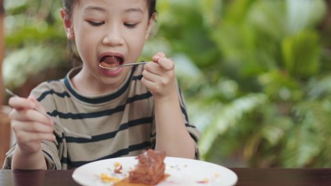Face focuing with blurred background of adorable asian girl kid is eating tasty chocolate cake. It shows happy and enjoy emotion of little child for eating delicious sweet or dessert in the cafe.
