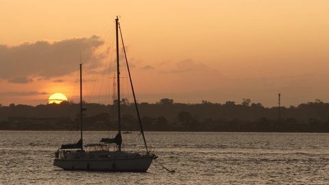 Beautiful sunset (or sunrise) on Maroni river. Big gold sun and orange sky behind a moored sailboat. France, French Guiana, Saint Laurent du Maroni.