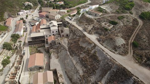 Aerial backward shot of the abandoned buildings and heaps of the former silver mines in Argentiera, Italy - end of the natural resources concept
