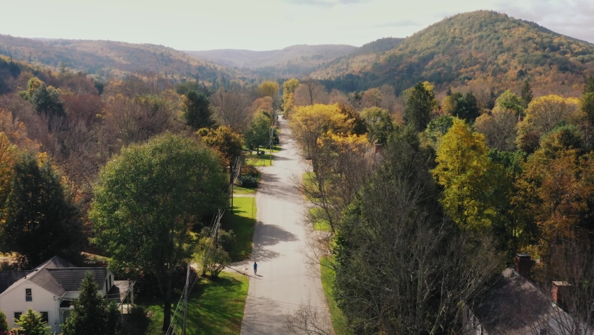 Aerial drone shot over a road with rows of ouses on both sides in Litchfield County, Connecticut, United States with the view of hilly terrain in the background.