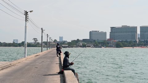 Pattaya , Chonburi , Thailand - 12 03 2021: A man raising his rod while reeling in his catch while fishing with others at the background is the city of Pattaya revealed at the Pattaya Fishing Dock, Ch