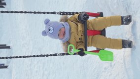 Happy toddler 15-20 months swinging on a swing in winter, slow motion. Vertical video