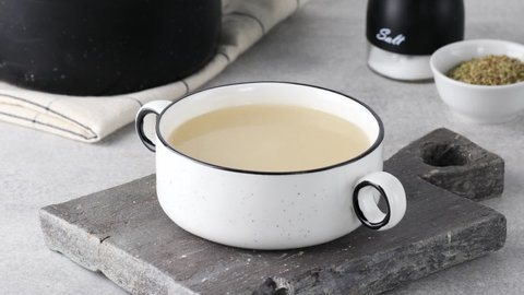 Pour a ladle of healthy homemade bone broth into a white bowl. 
