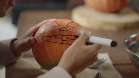 An adult lady is finishing to draw a jack face on a halloween pumpkin