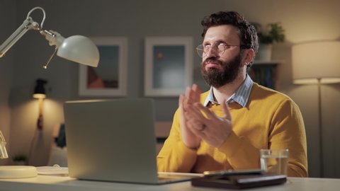 Sarcasm emotion, toxicity, man sarcastic applause. Gloomy skeptical bearded man in home office looking at computer screen and reluctantly claps her palms to create fake applause