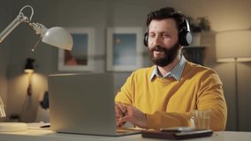 Man waving HELLO, greetings emotion. Positive smiling man with headphones in home office looking at computer webcam and waving his hand and says HELLO