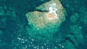 Slow flight over large rocks in the ocean. Aerial view of clear water in the sea. Large stones in the transparent clean water of the ocean Drone video. Ocean waves movement on stones top view.