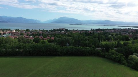 Red high-speed train moving on the background of Lake Garda video on drone. Red train moving between trees aerial view. Top view of a high-speed train in the background mountains in Italy side view.