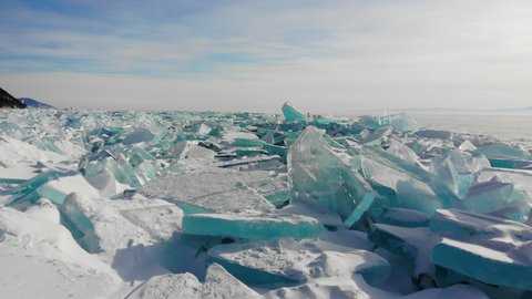 Large blocks of transparent ice near the shore of frozen Lake Baikal. Hummocks covered with snow. A sunny February day. Winter landscape.