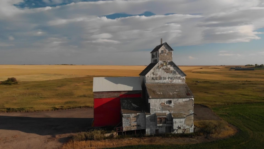 Drone backward shot of an old weathered grain elevator for storing wheat harvested on the rural area of Alberta, Canada on a cloudy evening.