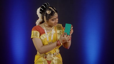 Indian bharatanatyam dancer showing by using green screen mobile phone by looking at camera - concept of online app advertisment, promotion and traditional culture.