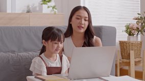 Asian young mother and her daughter using computer laptop watching online media or movie having fun together.Happiness Mom and little girl looking on laptop smile and laughing relax time at home