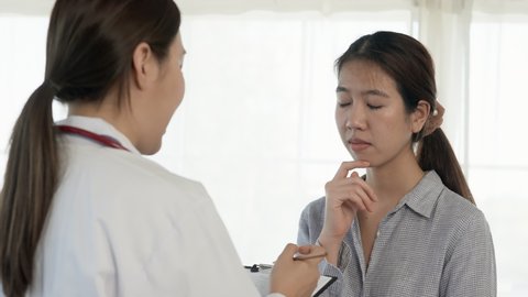 4K, Long-haired Asian woman patient discussing her illness with female doctor with stressed face, patient gesturing with chest pain, in hospital examination room. Concept Health and Medicine