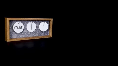 A wooden calendar block showing the date March 11th with a mans hand putting on and taking off the metal discs with the date and month on them, filmed in 8k quality 