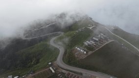 Beautiful 4K nature video footage of aerial view from drone of clouds and mist flowing on the mountains slopes,winding road,village and rural area. Fog and cloud inversion over the mountains.