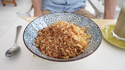 Bowl with granules and coconut and chocolate chips for a healthy breakfast. Male hand with a spoon and a plate with muesli in a cafe in the morning, close up